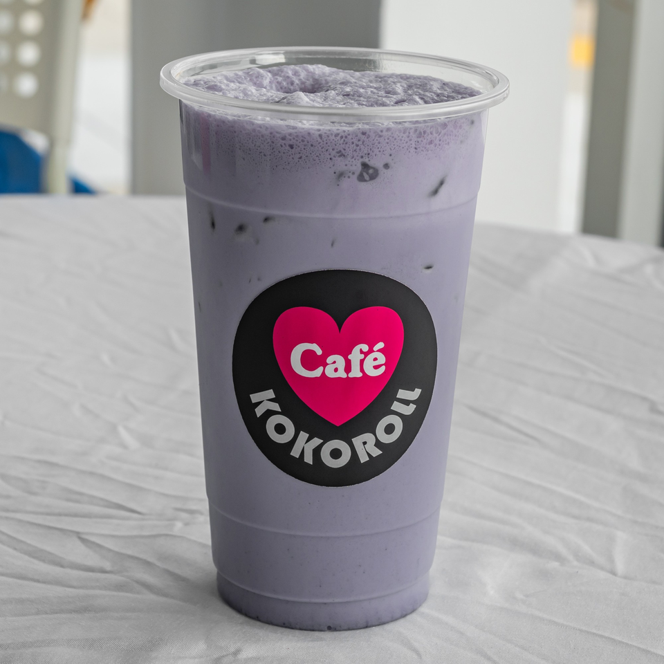 A KOKOROLL Cafe taro boba drink with foam and ice, on a white tablecloth.