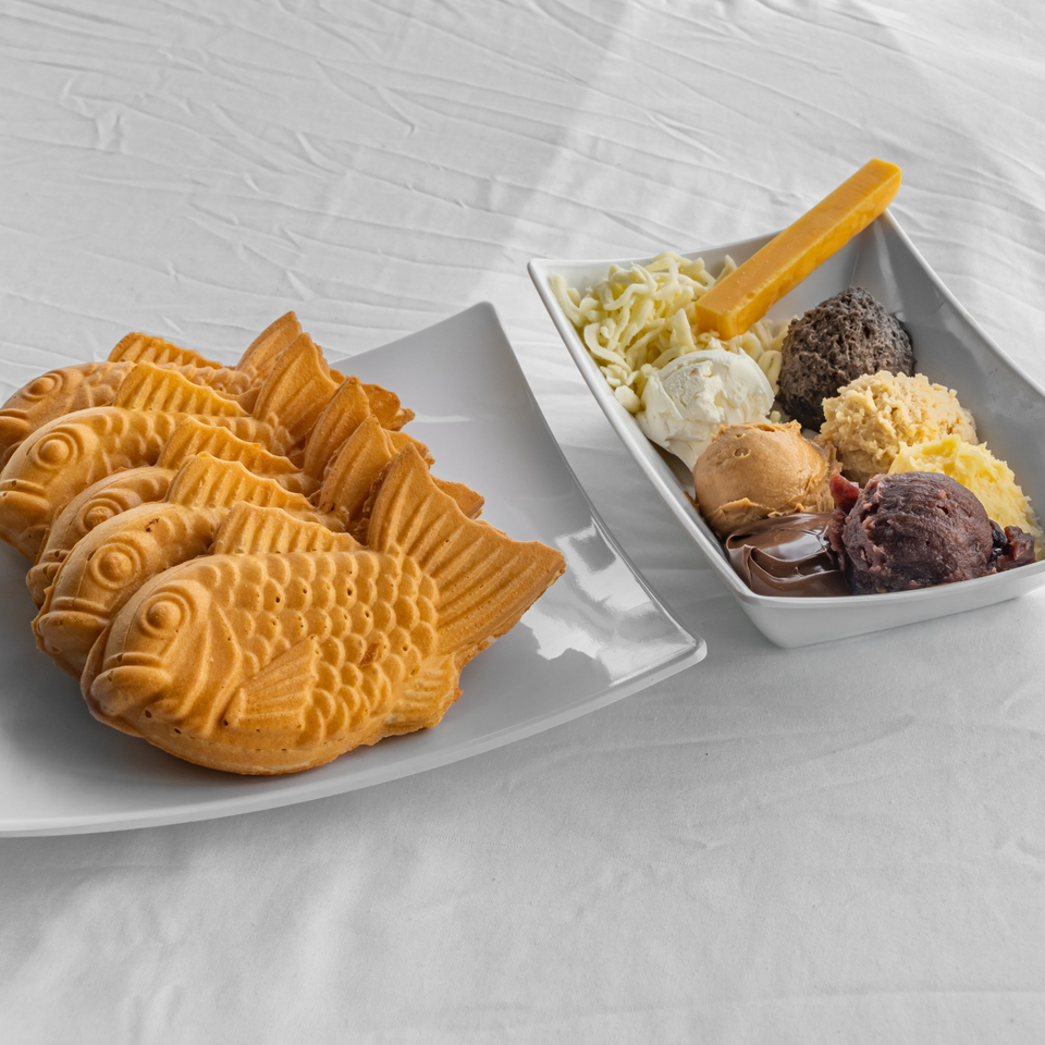 Taiyaki fish-shaped cakes on a plate next to a bowl of ice cream scoops and toppings.