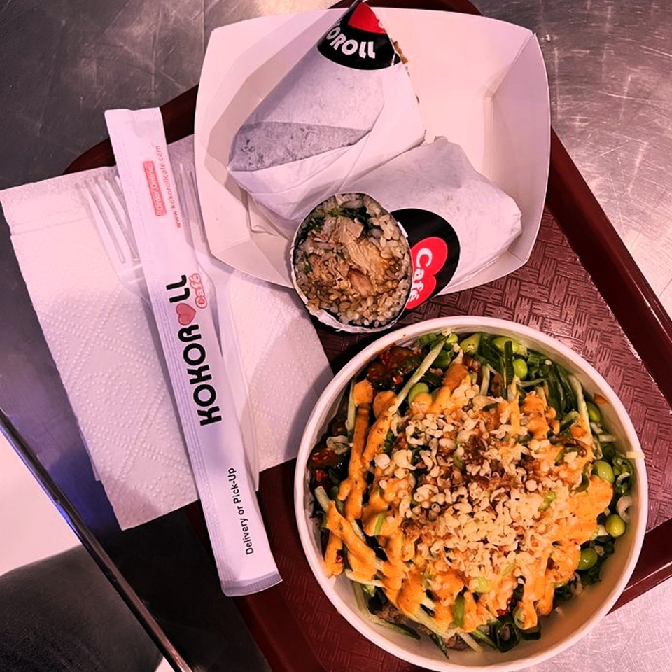KOKOROLL poke bowl with sauce and nuts, two wrapped sushi burritos, and branded chopsticks on a tray.
