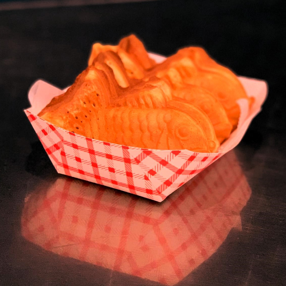 Golden-brown taiyaki, fish-shaped pastries, served in a red and white checkered paper tray.