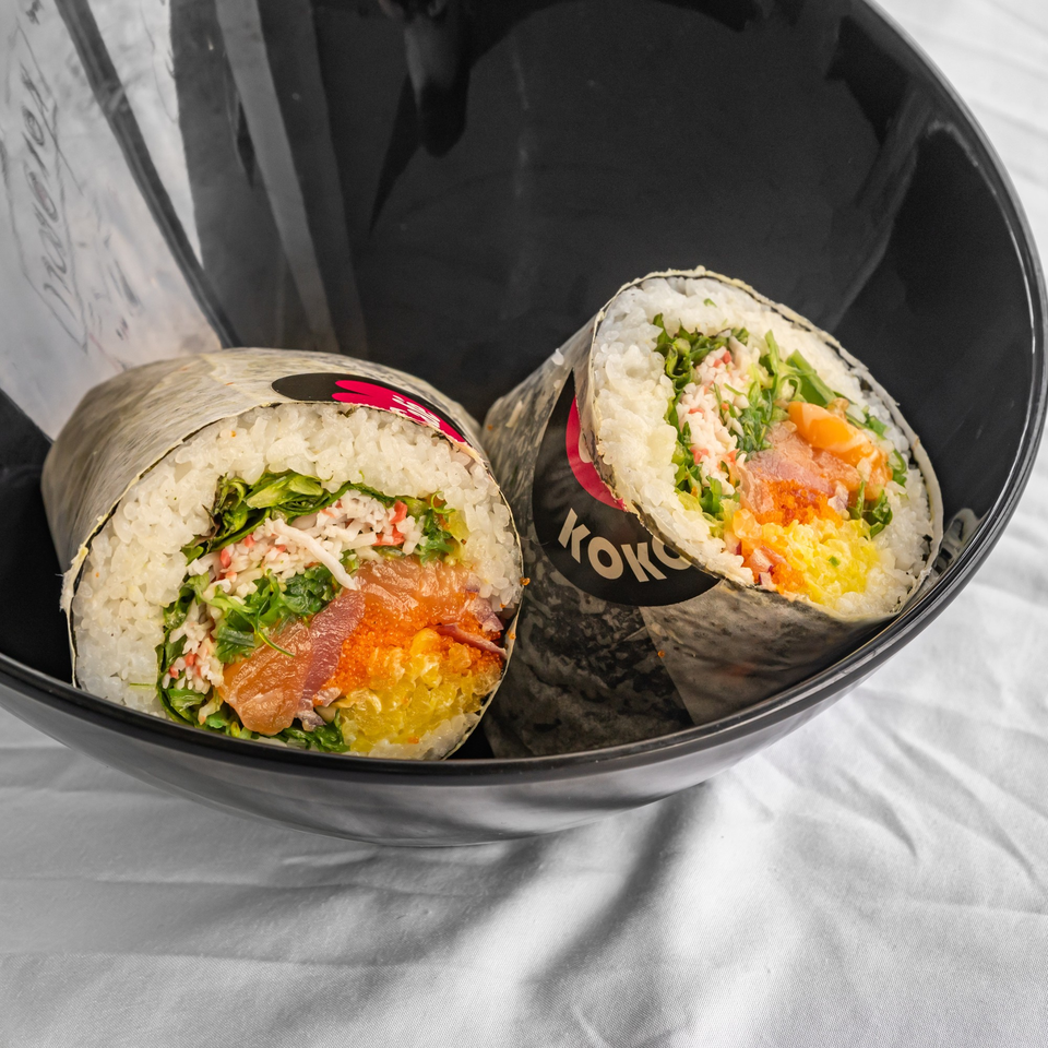 Two KOKOROLL sushi burritos, filled with salmon, crab, roe, and greens, in a black bowl.