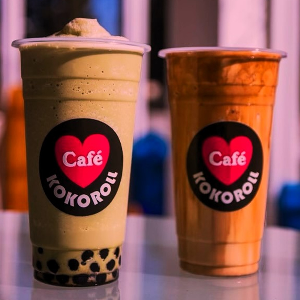 Two KOKOROLL Cafe bubble tea drinks, one green with boba and one orange, on a counter.