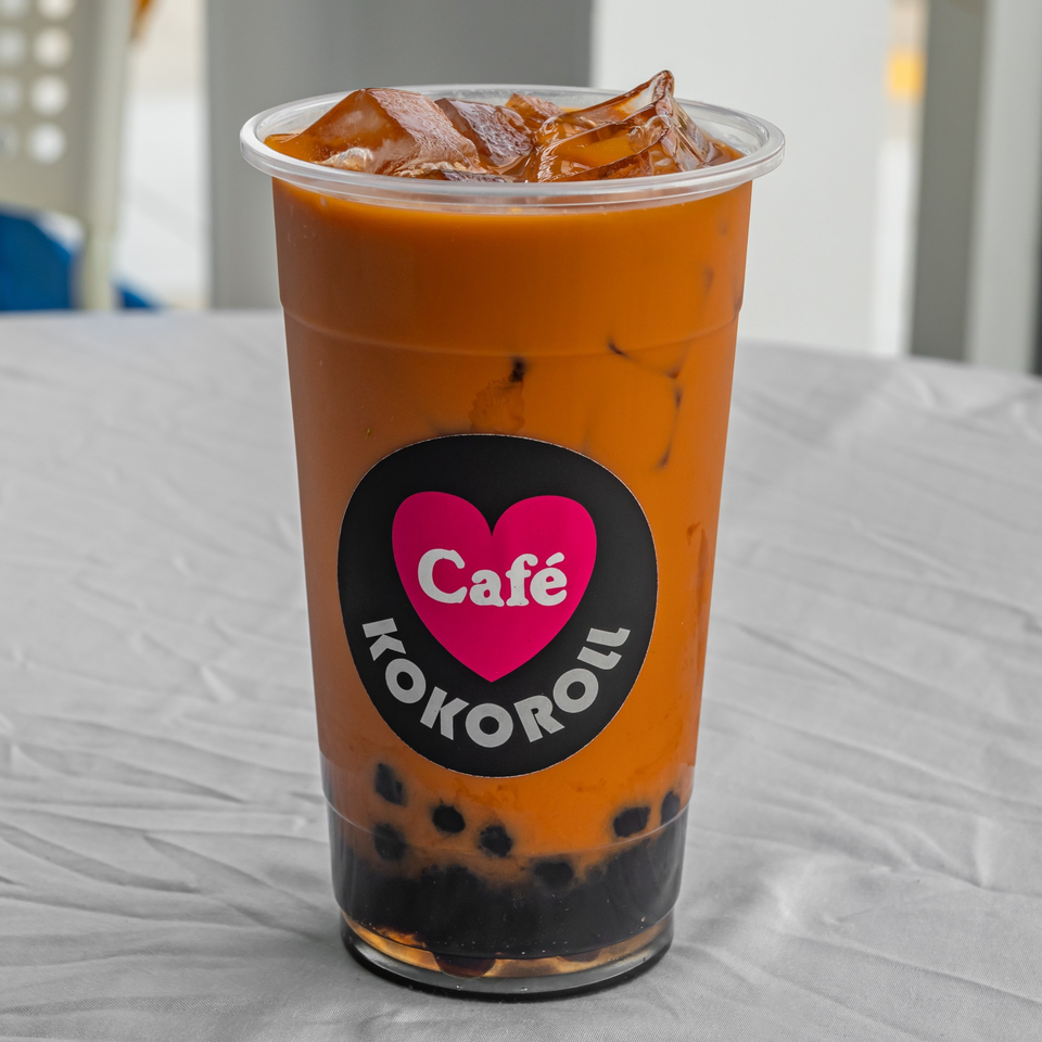 KOKOROLL Cafe Thai iced tea with boba and ice in a clear plastic cup.
