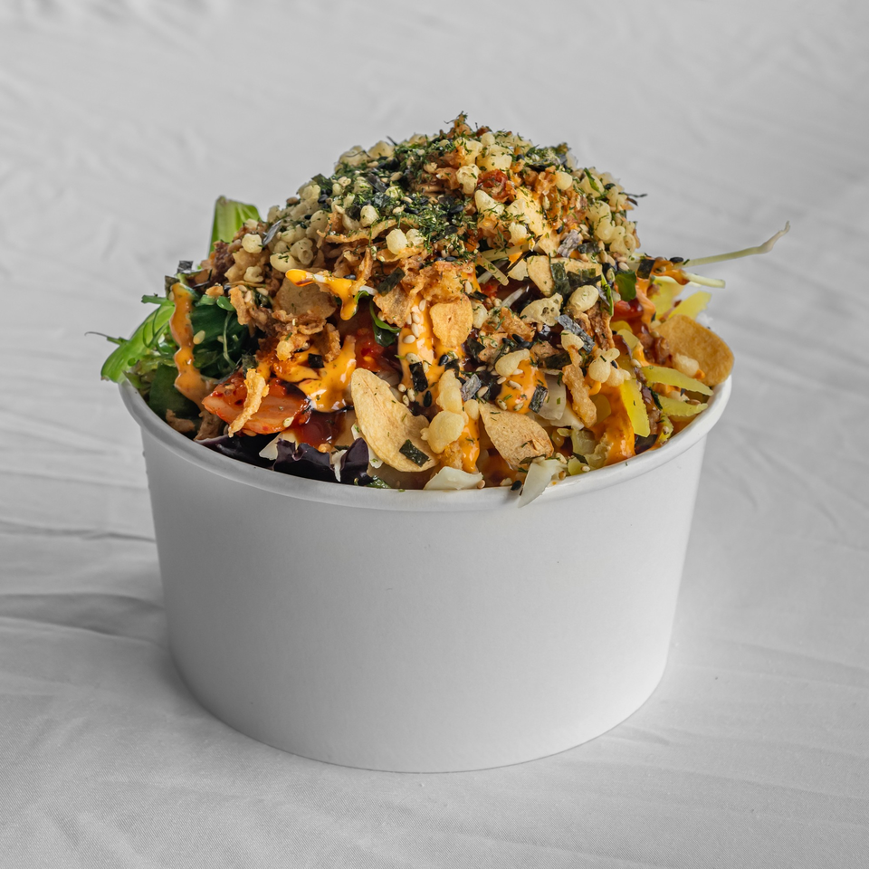 A KOKOROLL Poke & Ramen poke bowl, overflowing with toppings and drizzled with sauce.