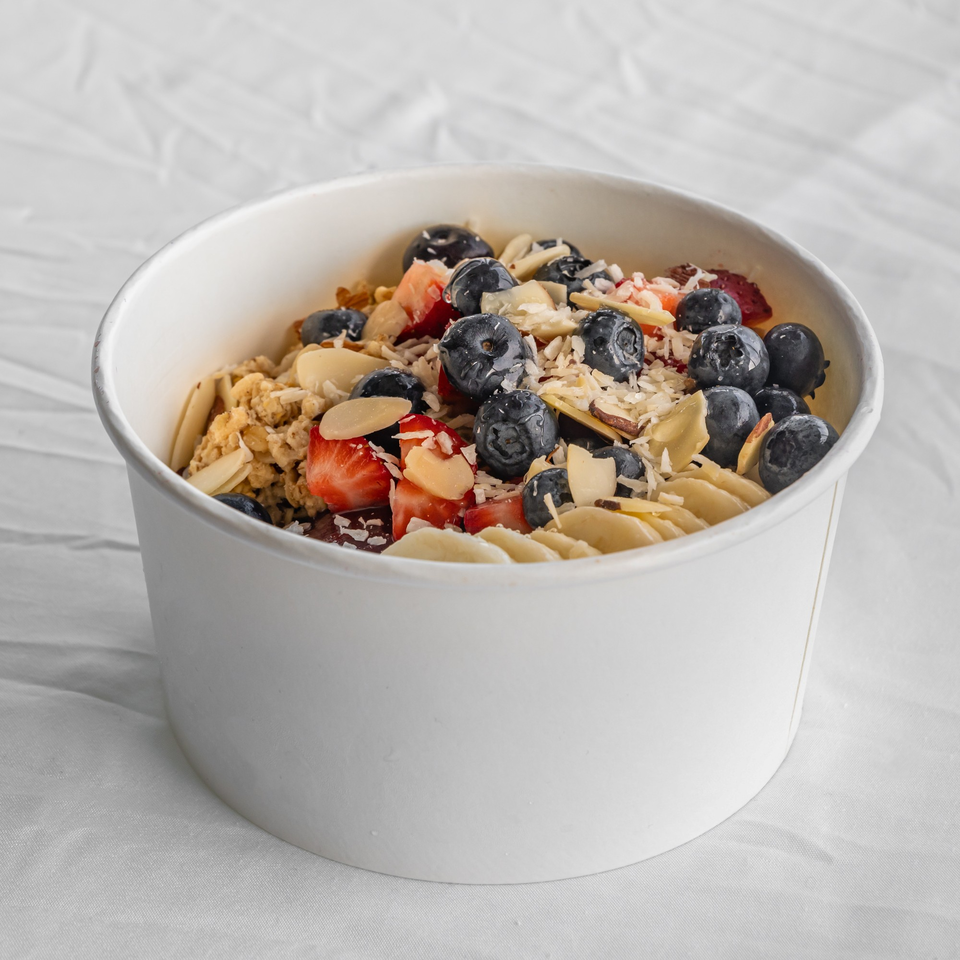A white bowl filled with granola, blueberries, strawberries, and sliced almonds on a white surface.