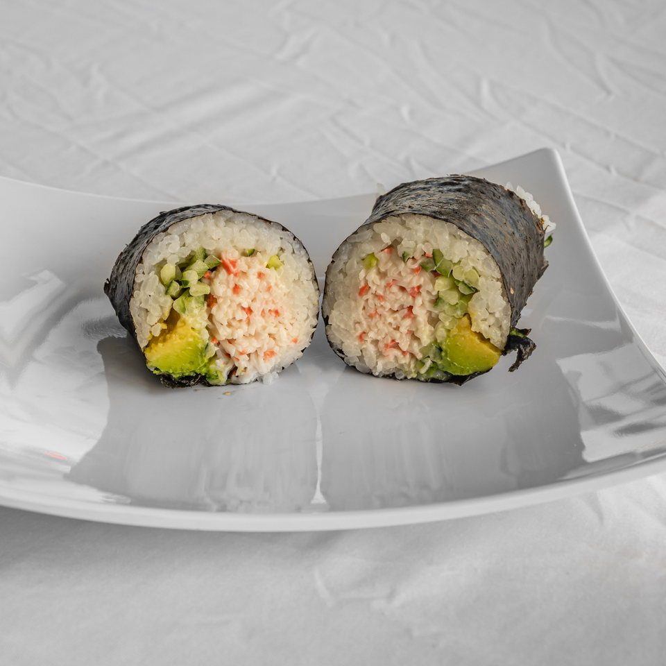 Two halves of a KOKOROLL poke roll with crab, avocado, and cucumber on a white plate.