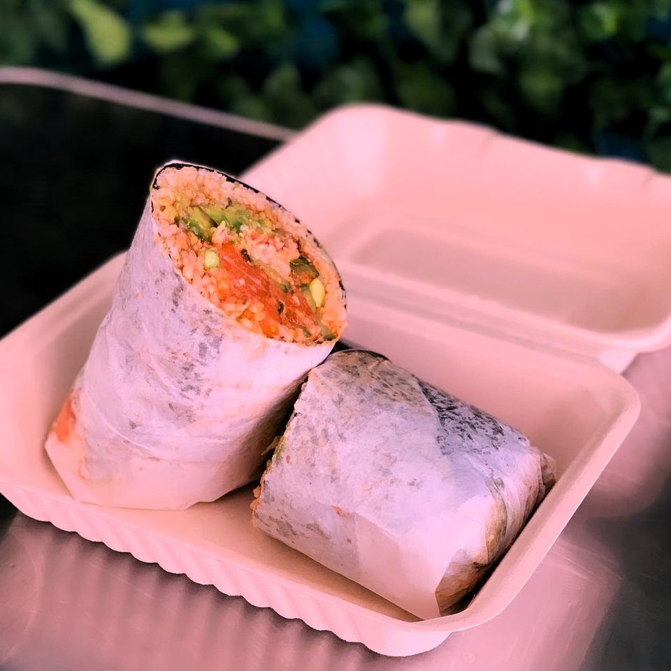 Two KOKOROLL poke burritos, one cut in half to show salmon, avocado, and rice, in a takeout container.