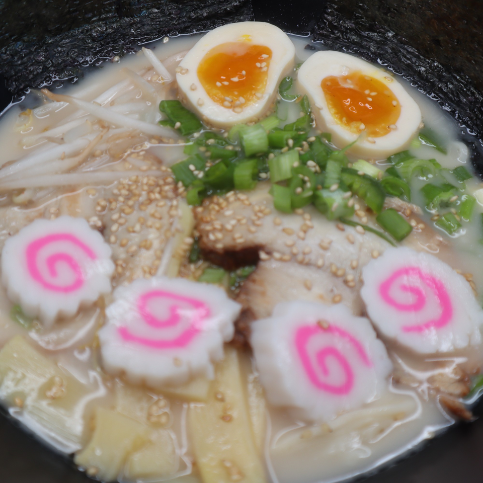 KOKOROLL's ramen bowl with soft-boiled eggs, fish cakes, green onions, and sesame seeds.